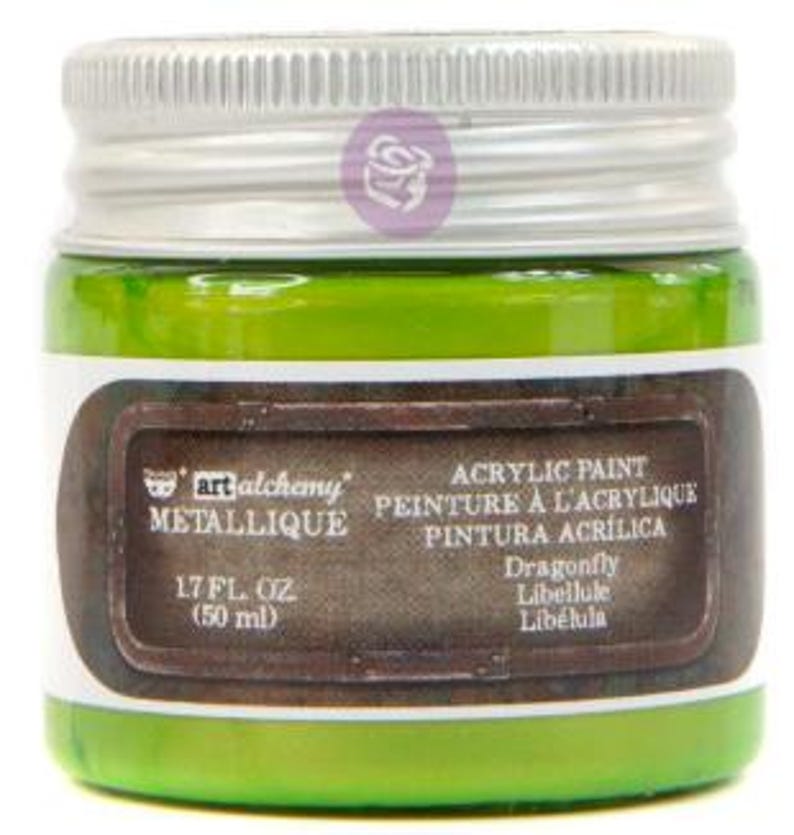 May include: A small glass jar of bright green Art Alchemy Metallique acrylic paint with a silver screw-top lid. The label features the text '1.7 FL. OZ. (50 ml)', 'ACRYLIC PAINT', and the colour name 'Dragonfly' in a dark brown rectangular frame.