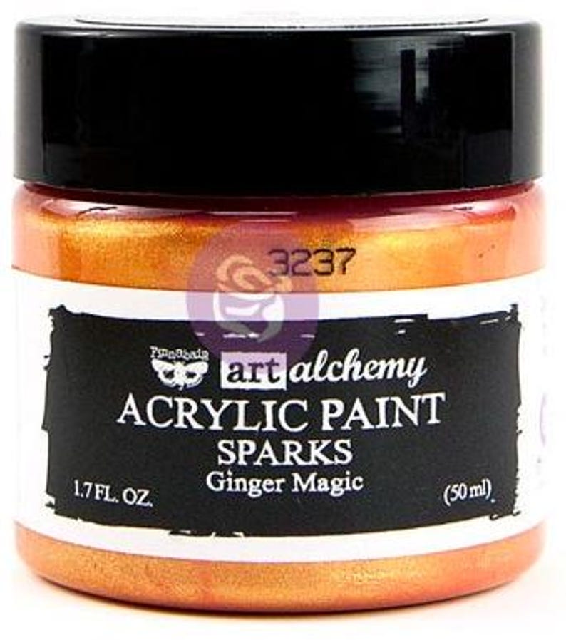 May include: A jar of Art Alchemy Sparks acrylic paint in the colour Ginger Magic. The jar has a black lid and a label with the text 3237, Finnabair, art alchemy, ACRYLIC PAINT, SPARKS, Ginger Magic, 1.7 FL. OZ., and 50 ml. The paint is orange.