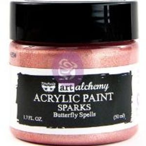 May include: A jar of Art Alchemy Sparks acrylic paint in the colour Butterfly Spells. The jar has a black lid and a label with white text reading Art Alchemy Acrylic Paint Sparks Butterfly Spells, 1.7 fl. oz., and 50 ml. The paint is metallic pink.