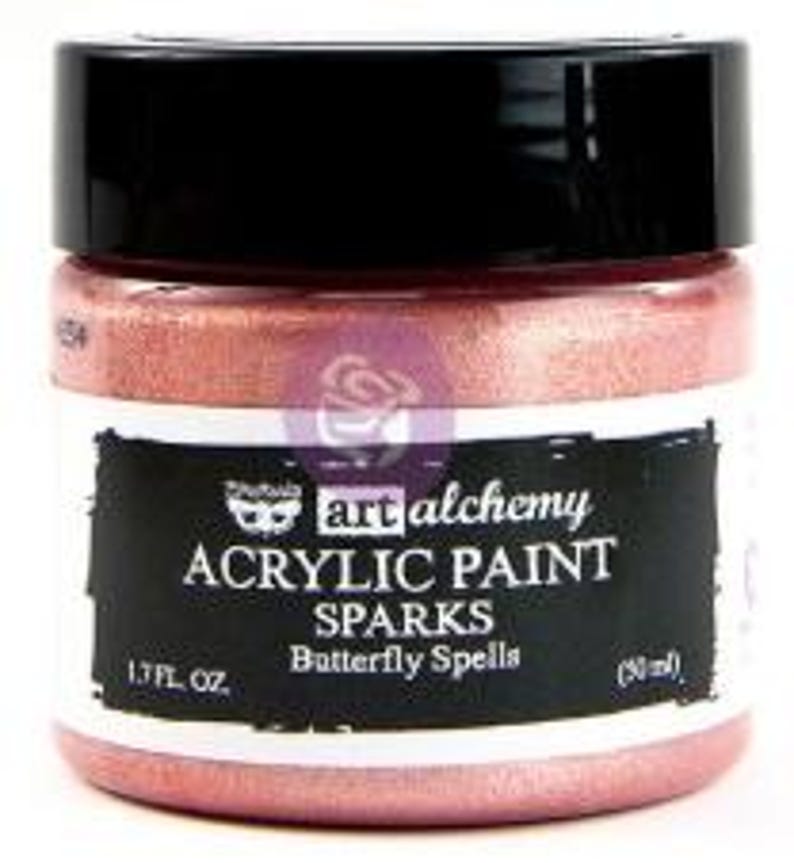 May include: A jar of Art Alchemy Sparks acrylic paint in the colour Butterfly Spells. The jar has a black lid and a label with white text reading Art Alchemy Acrylic Paint Sparks Butterfly Spells, 1.7 fl. oz., and 50 ml. The paint is metallic pink.
