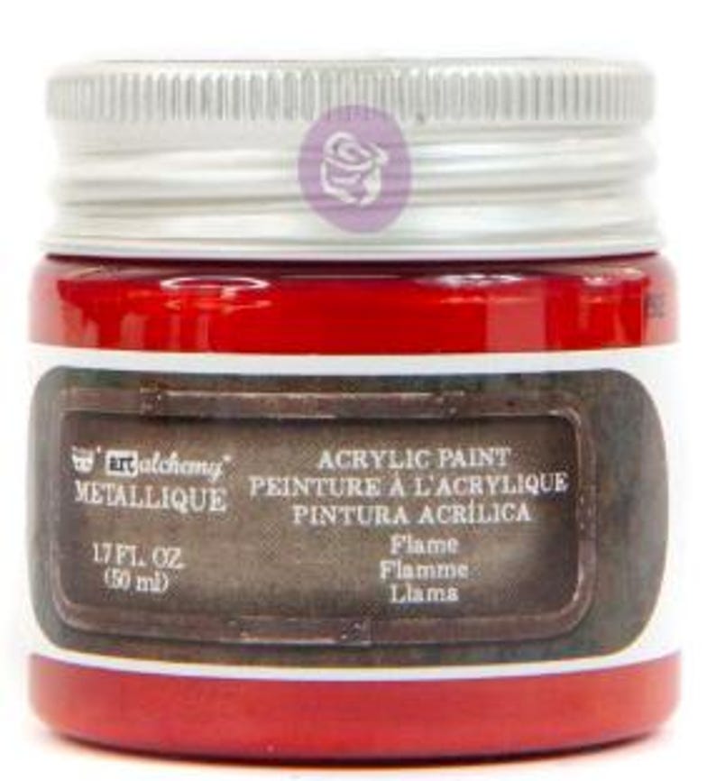 May include: A small jar of Art Alchemy Metallique acrylic paint in the colour Flame. The jar has a silver screw-top lid and a label that reads 1.7 fl. oz. (50 ml). The paint inside is a vibrant red colour, and the label features a dark brown border.