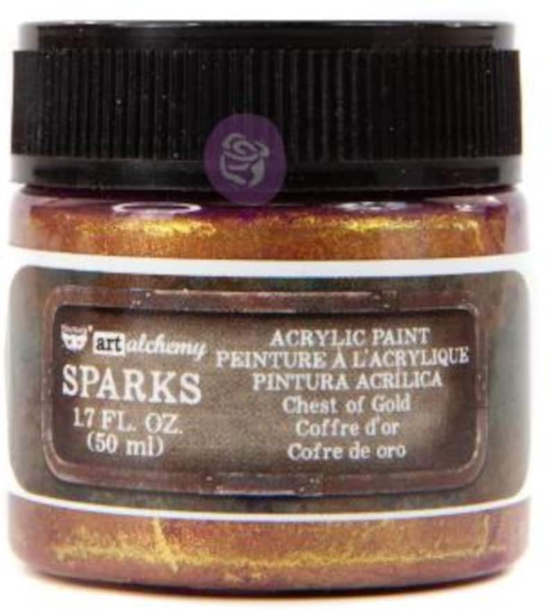 May include: A jar of Art Alchemy Sparks acrylic paint in the colour Chest of Gold. The jar has a black ribbed lid and a label that reads Sparks, 1.7 fl. oz. (50 ml), Acrylic Paint, and Chest of Gold. The paint inside is a metallic gold hue.
