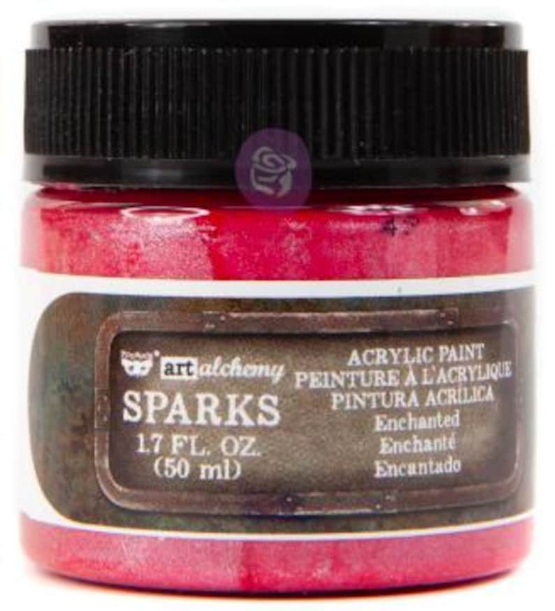 May include: A small jar of bright pink acrylic paint with a black ribbed screw-top lid. The label features the text Art Alchemy Sparks, 50 ml (1.7 fl. oz.), and the colour name Enchanted. The container is cylindrical with a clear glass base.