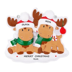 May include: Personalized Christmas ornament featuring two moose wearing Santa hats. The moose are sitting together and the ornament says "Merry Christmas" and "Year". The moose are labeled "Mom" and "Olivia".