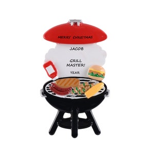 May include: A red and black grill Christmas ornament with a white label that says "Merry Christmas Jacob Grill Master! Year". The grill has a hamburger, hot dogs, corn on the cob, and other grilling items on it.