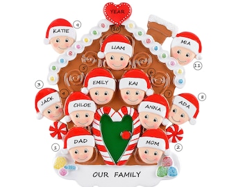 May include: A gingerbread house Christmas ornament with 11 faces of family members, including "Dad", "Mom", "Liam", "Emily", "Kai", "Anna", "Ada", "Chloe", "Jack", "Katie", and "Mia". The ornament has a red heart with candy canes on either side and the words "Our Family" at the bottom.