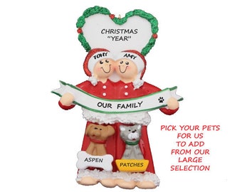 May include: Personalized Christmas ornament featuring a couple in red and white pajamas holding a banner that reads "Our Family". The ornament also includes two pets, a dog and a cat, with their names "Aspen" and "Patches" written below them. The ornament is decorated with a green wreath heart with the text "Christmas "Year"".