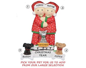 May include: Personalized Christmas ornament featuring a couple in red and white pajamas with a cat and two dogs. The ornament includes the names "Tony", "Katie", "Patches", "Buddy", and "Aspen".