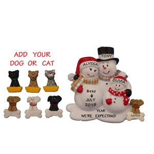 May include: A white snowman family Christmas ornament with the names Tony, Alyssa, and Olivia. The snowman couple is holding a sign that says "Baby July 2019 Year We're Expecting!" and a small snowman with the name Aspen is holding a bone.
