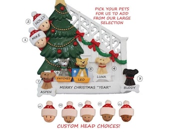Könnte beinhalten: Ein weißer Weihnachtsbaumschmuck mit einem grünen Weihnachtsbaum, einem weißen Haus mit einer roten Schleife und einer Familie von Menschen und Haustieren. Der Anhänger hat den Text "Frohe Weihnachten "Jahr"" und "Wählen Sie Ihre Haustiere aus, die wir aus unserer großen Auswahl hinzufügen sollen".
