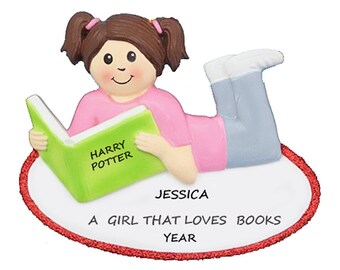May include: A personalized Christmas ornament featuring a girl with brown hair and pigtails lying down and reading a green book with the words "Harry Potter" on the cover. The ornament has a red oval border with the text "Jessica, A girl that loves books, YEAR".