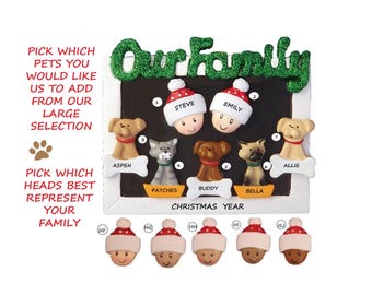 May include: A personalized Christmas ornament featuring a white frame with the words "Our Family" in green glitter letters. The frame contains images of a family with their pets, including a cat, dog, and a couple. The ornament also includes a space for the year.