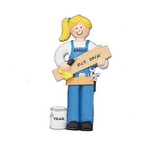 May include: A figurine of a blonde woman wearing blue overalls, holding a drill and a wooden plank that reads "D.I.Y. DIVA!". The figurine also has a tool belt, a paint can that says "YEAR", and the name "EMILY" on the overalls.