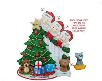 May include: A Christmas ornament featuring a green Christmas tree, three figures wearing Santa hats, and a teddy bear. The ornament has the text "Merry Christmas" and "Pick your pet for us to add from our large selection."