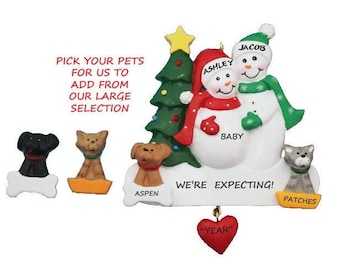 May include: A personalized Christmas ornament featuring a snowman couple with a baby bump, a Christmas tree, and two dogs and a cat. The ornament says "We're Expecting!" and "Baby".