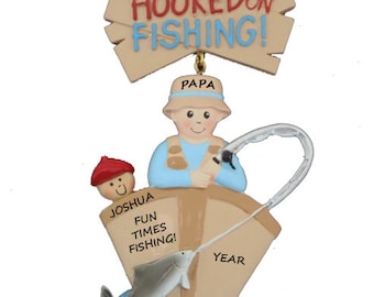 May include: A personalized Christmas ornament featuring a cartoon fisherman holding a fishing rod and a fish. The ornament is decorated with the words "Hooked on Fishing!" and "Fun Times Fishing!" along with the names "Papa", "Joshua", and "Clear Lake".