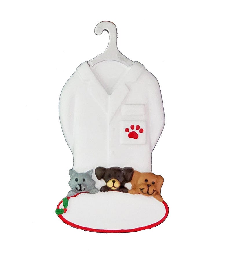 May include: White ceramic ornament shaped like a veterinarian's coat with a red paw print on the pocket. Three small ceramic animals, a grey cat and two brown dogs, are peeking out from behind the coat. The ornament has a blank oval space for personalisation.