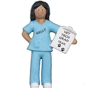May include: A blue and white ornament of a female veterinary technician holding a clipboard that says "Vet Tech Grad Year" with paw prints. The ornament has the name "Kelly" on the shirt.