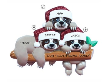 May include: A Christmas bauble featuring three sloths wearing Santa hats. The sloths are on a branch with the text "OUR "SLOTH"SOME FAMILY" and the names "MOM", "SOPHIE", and "JASON".