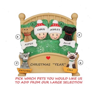 May include: A Christmas ornament featuring a bed with two figures wearing Santa hats, and four pets. The ornament has the text "Christmas Year" and the names of the pets. The image also includes the text "Pick which pets you would like us to add from our large selection."
