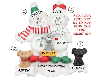 May include: Personalized snowman Christmas ornament with the names David and Katie, a cat named Patches, and two dogs named Aspen and Buddy. The ornament says "We're expecting!" and includes a space for the year.