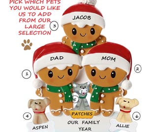May include: A personalized family Christmas ornament featuring gingerbread people with red Santa hats and green scarves. The ornament includes the names "Dad", "Mom", and "Jacob", with space for pets "Aspen", "Patches", and "Allie".
