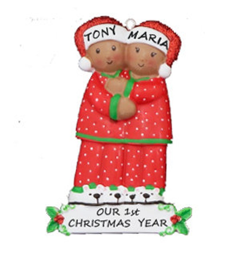 Puede incluir: Adorno navide&ntilde;o personalizado con una pareja en pijama rojo con lunares blancos, abraz&aacute;ndose. El adorno tiene los nombres "Tony" y "Maria" en los sombreros y el texto "Nuestro 1er a&ntilde;o de Navidad" en la base.