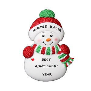 May include: White snowman Christmas ornament with a red and green striped scarf and hat. The hat has the text "Auntie Katie" on it. The snowman has a red heart and the text "Best Aunt Ever!" on the front.