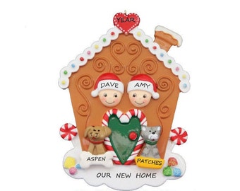 May include: A gingerbread house Christmas ornament with a red heart on the roof, two people peeking out the windows, and two pets, a dog and a cat, standing in front of the house. The text on the ornament reads "YEAR", "DAVE", "AMY", "ASPEN", "PATCHES", "OUR NEW HOME", and "PICK WHICH PETS YOU WOULD LIKE US TO ADD!"