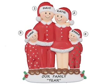 Puede incluir: Un adorno navideño rojo y blanco con una familia de cuatro personas en pijamas a juego. El adorno está personalizado con los nombres "Dave", "Katie", "Liam" y "Emma". El texto "Nuestra familia "Año"" también está incluido en el adorno.
