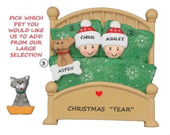 May include: Personalized Christmas ornament featuring a couple in bed with a dog. The ornament is beige and green with the names "Chris" and "Ashley" and the dog's name "Aspen". The text "Christmas "Year"" is at the bottom of the ornament.