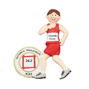 May include: A personalized Christmas ornament featuring a male runner in a red tank top and white shorts. The ornament includes a gold medal with the text "REDDING MARATHON", "26.2", and "4:21". The runner's bib reads "TRAVIS YEAR".