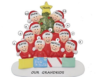 May include: A Christmas tree ornament featuring a green glitter Christmas tree with 11 red-suited figures, each with a name and a number. The ornament reads "OUR GRANDKIDS" at the bottom.