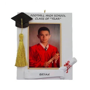 May include: White graduation ornament with a photo frame, a black graduation cap, a gold tassel, and a diploma scroll. The text on the ornament reads "FOOTHILL HIGH SCHOOL CLASS OF "YEAR"" and "BRYAN".