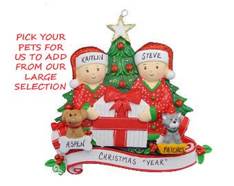 May include: Personalized Christmas ornament featuring a couple in pajamas with a Christmas tree, a gift box, and two pets. The ornament is decorated with holly and a banner that reads "Christmas "YEAR"".