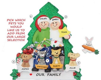 May include: A personalized Christmas ornament featuring a couple standing in front of a green glitter Christmas tree with a star on top. The couple is holding a string of lights and there are four pets in front of them. The ornament says "Our Family" at the bottom.