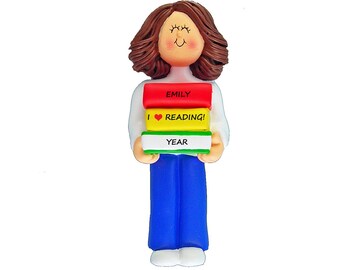 May include: A personalized ornament of a teacher holding books. The books are stacked and say "Emily", "I love reading!" and "Year". The teacher has brown hair and is wearing a white shirt and blue jeans.