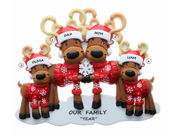 May include: A Christmas ornament featuring a family of reindeer. Each reindeer wears a red sweater with white snowflakes and a Santa hat. The ornament includes the names "Dad", "Mom", "Olivia", and "Liam". The text "OUR FAMILY" and "YEAR" are also present.