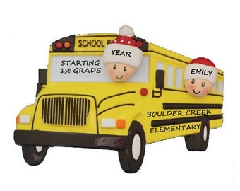 Könnte beinhalten: Gelber Schulbus-Weihnachtsbaumschmuck mit zwei Kindern, die Weihnachtsmützen tragen. Der Bus trägt den Text "School Bus", "Starting 1st Grade", "Boulder Creek Elementary" und "Year".