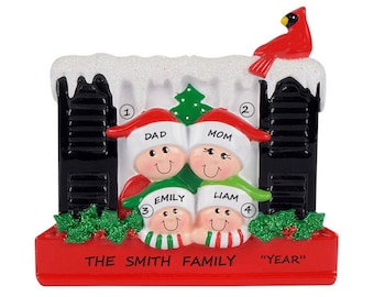 Puede incluir: Un adorno navideño rojo, blanco y verde que representa a una familia de cuatro personas de pie frente a una casa en blanco y negro con un cardenal rojo en el techo. El adorno dice "The Smith Family" y "Year".