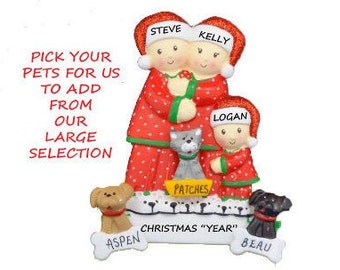 May include: Personalized Christmas ornament featuring a family of three in red and green pajamas with a cat and two dogs. The ornament says "PICK YOUR PETS FOR US TO ADD FROM OUR LARGE SELECTION" and "CHRISTMAS "YEAR"".