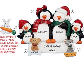 May include: A Christmas ornament featuring a family of four penguins with names Ashley, Steve, Ryan, and Mia. The penguins are wearing red and green hats and scarves. The ornament also includes a dog named Aspen and a cat named Patches. The ornament says "Christmas Year" at the bottom.