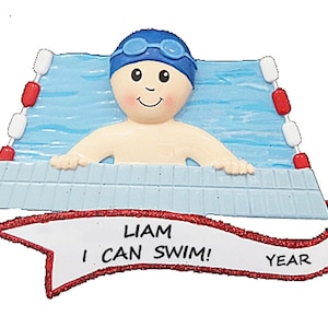 May include: A blue and white personalized Christmas ornament featuring a boy wearing a blue swim cap and goggles, holding onto the side of a swimming pool. The ornament has a red banner with the text "Liam I CAN SWIM! YEAR".