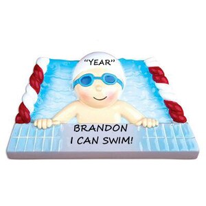 May include: A personalized Christmas ornament featuring a cartoon swimmer in a pool. The ornament is white with blue and red accents. The swimmer is wearing a white swim cap with the text "YEAR" on it. The text "BRANDON I CAN SWIM!" is printed below the swimmer.