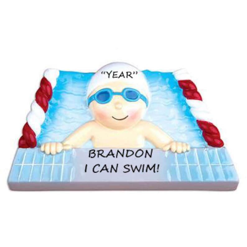 May include: A personalized Christmas ornament featuring a cartoon swimmer in a pool. The ornament is white with blue and red accents. The swimmer is wearing a white swim cap with the text "YEAR" on it. The text "BRANDON I CAN SWIM!" is printed below the swimmer.