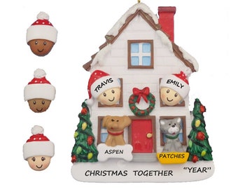 May include: A white house-shaped Christmas ornament with a red door and a wreath. There are two figures with Santa hats peeking out of windows, a dog and a cat in other windows, and the names "Travis", "Emily", "Aspen", and "Patches" written on the ornament. The text "Christmas Together "Year" is written at the bottom.