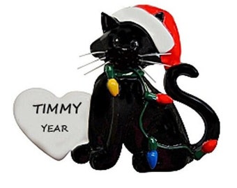 May include: Black cat Christmas ornament wearing a Santa hat and holding a string of lights. The ornament has a white heart-shaped tag with the text "TIMMY YEAR".
