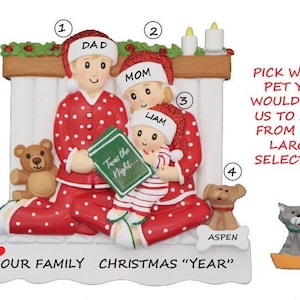 May include: A personalized Christmas ornament featuring a family of three in red and white pajamas, sitting by a fireplace. The ornament includes the names "Dad", "Mom", and "Liam". The text "Twas the Night..." is visible on a book. The ornament also includes a dog and a cat, with the text "Pick which pet you would like us to add from our large selection".
