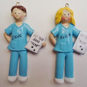 May include: Two personalized ornaments of a male and female vet tech wearing blue scrubs and holding a clipboard with the text "Vet Tech Grad "Year"". The male ornament has the name "Steve" and the female ornament has the name "Alicia".
