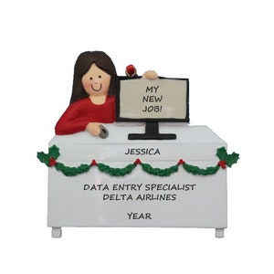 May include: A white desk with a computer monitor, keyboard, and mouse. A woman is sitting at the desk and holding a sign that says "My New Job!" The desk has a nameplate that says "Jessica" and the text "Data Entry Specialist Delta Airlines Year".